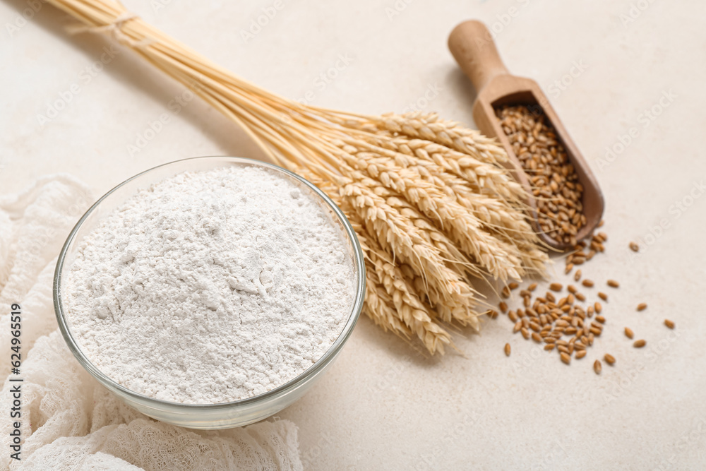 Wheat flour in glass bowl and spikelets on light background