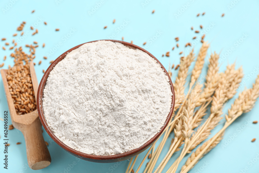 Bowl with wheat flour and spikelets on blue background