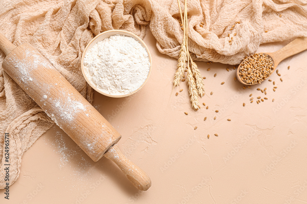 Flour, wheat and rolling pin on beige background