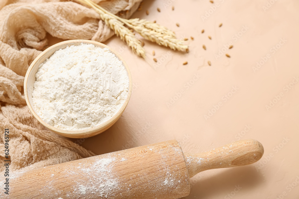 Flour, wheat and rolling pin on beige background