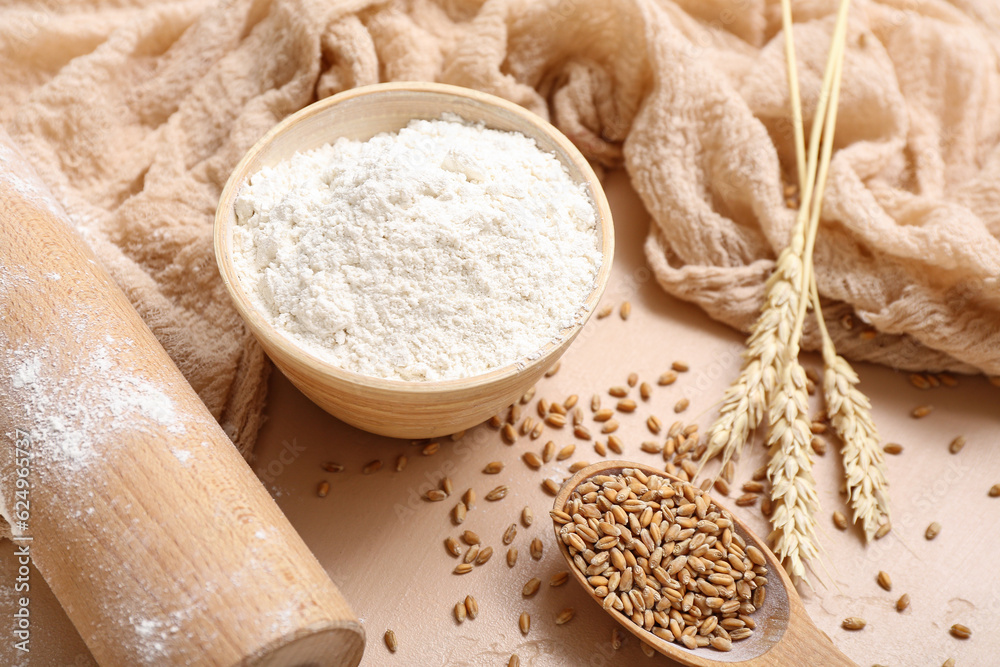 Flour, wheat and rolling pin on beige background