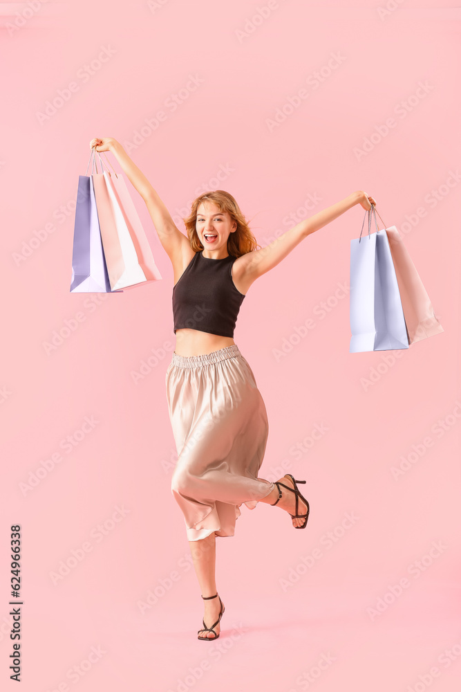 Beautiful happy young woman with shopping bags on pink background