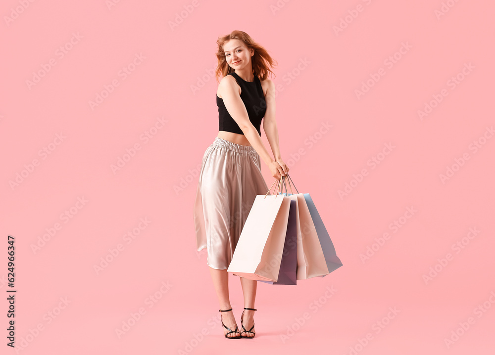 Beautiful happy young woman with shopping bags on pink background