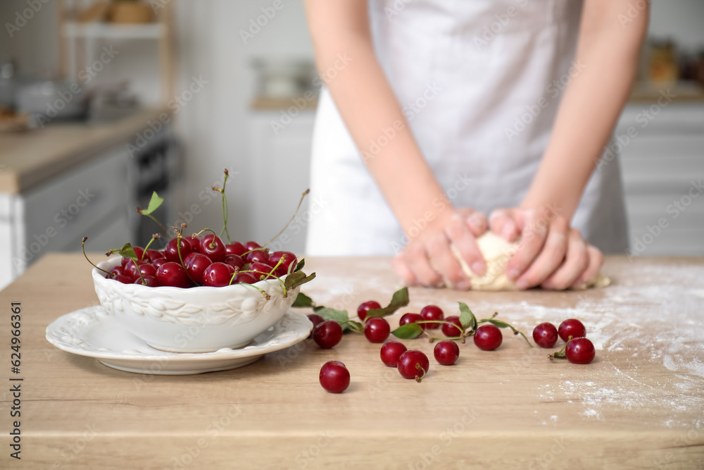 Bowl with cherries and woman kneading dough in kitchen, closeup