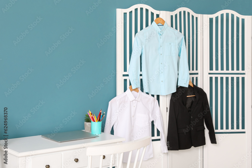 Stylish school uniform hanging on folding screen in room