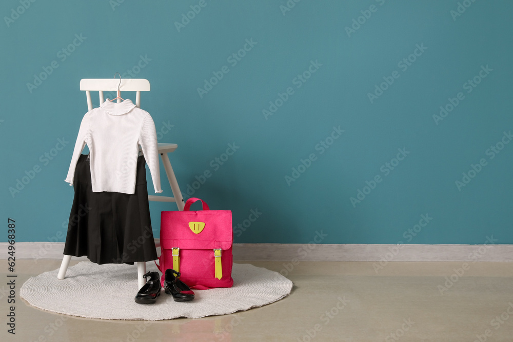 Chair with stylish school uniform, shoes and backpack near color wall in room