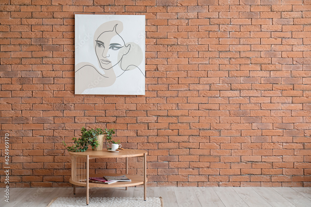 Wooden table with cup of coffee and home decor in room near brick wall