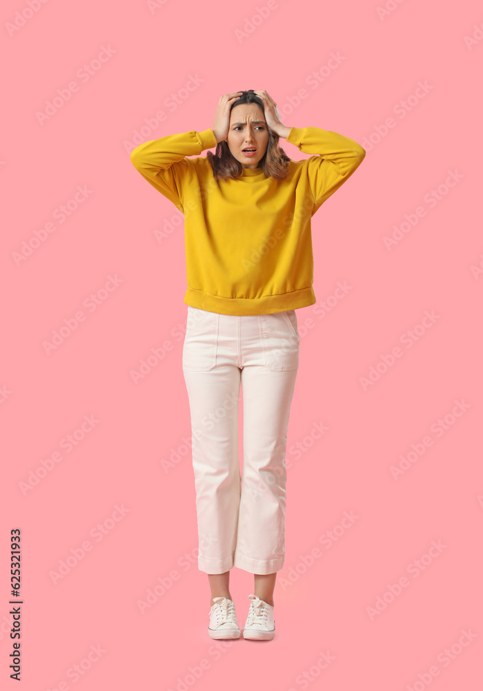 Stressed young woman in yellow sweatshirt on pink background