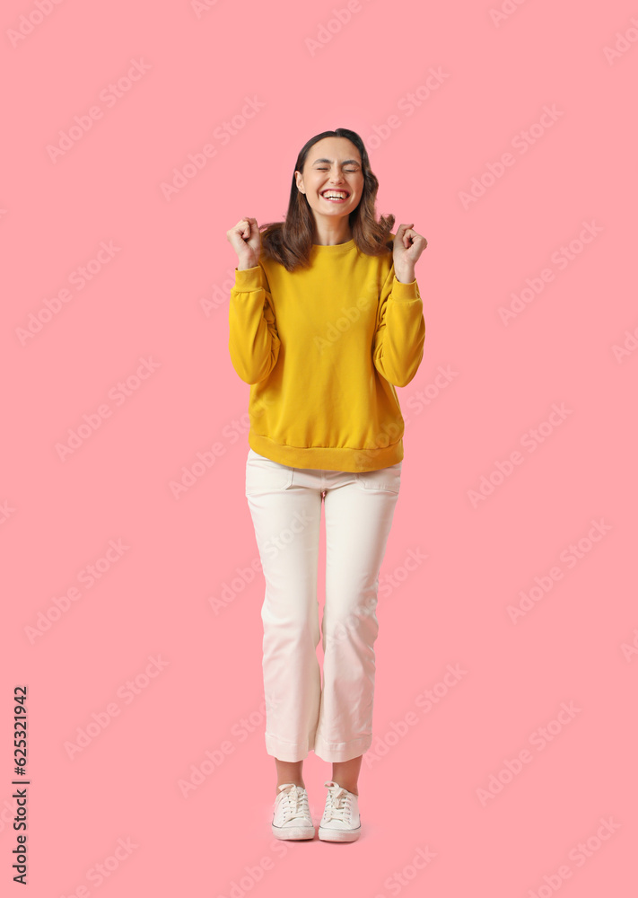 Happy young woman in yellow sweatshirt on pink background