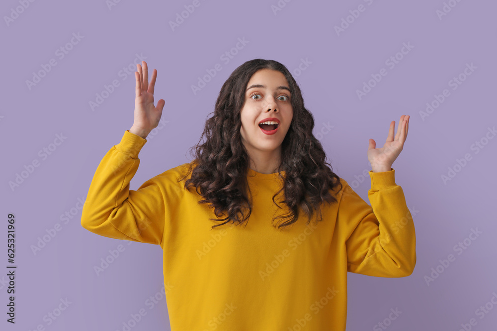 Surprised teenage girl in yellow sweatshirt on lilac background