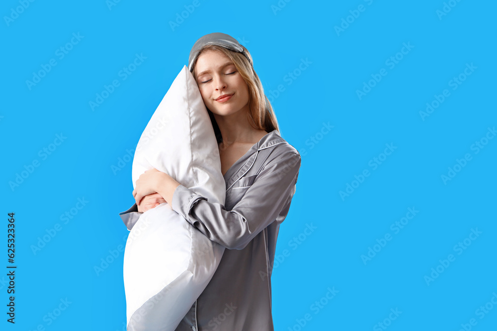 Young woman in pajamas with pillow on blue background