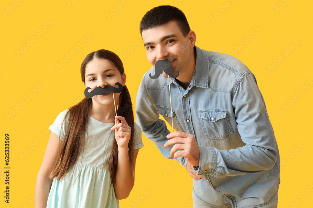 Portrait of father and his little daughter with paper mustache on yellow background