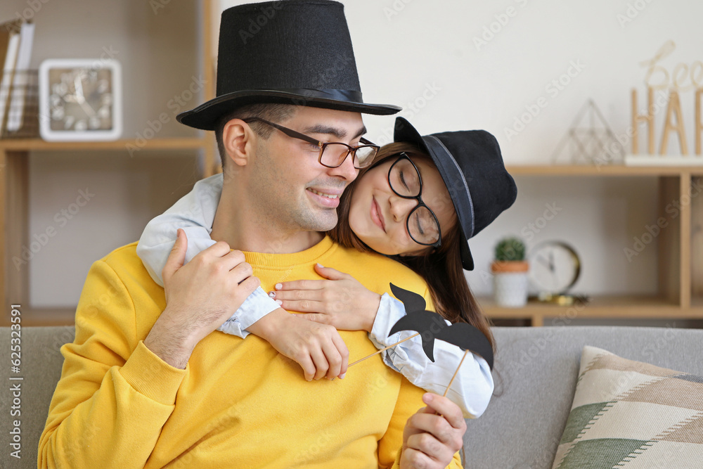 Portrait of father and his little daughter with paper mustache, hats and glasses at home