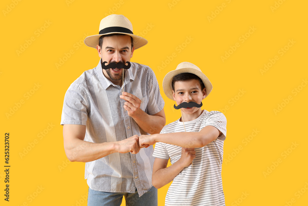 Portrait of father and his little son with paper mustache bumping fists on yellow background