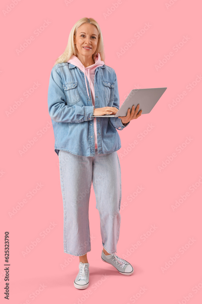 Mature female programmer working with laptop on pink background