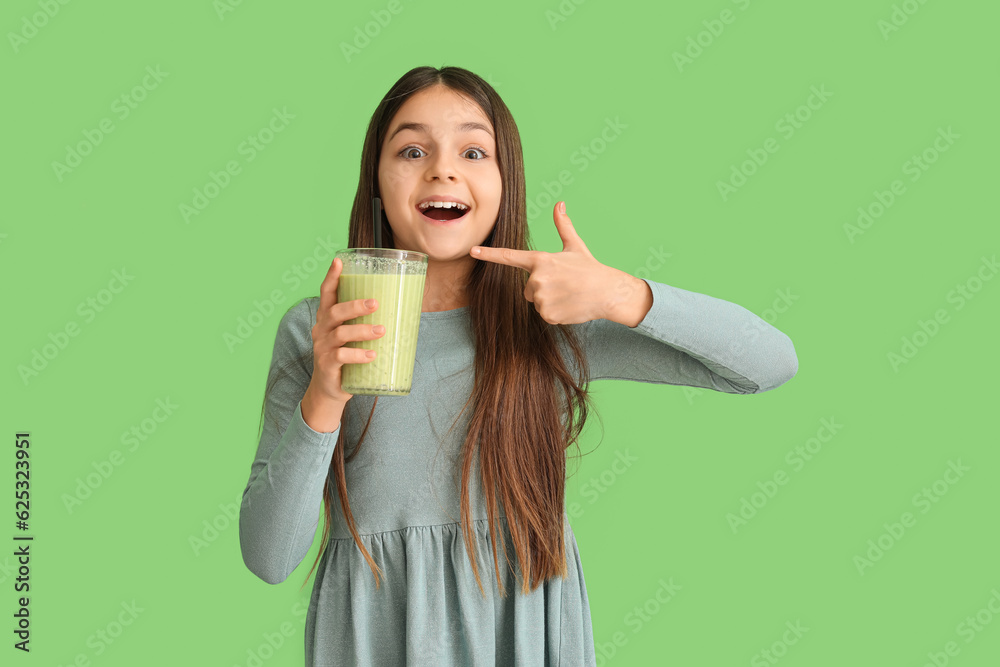 Little girl pointing at glass of smoothie on green background