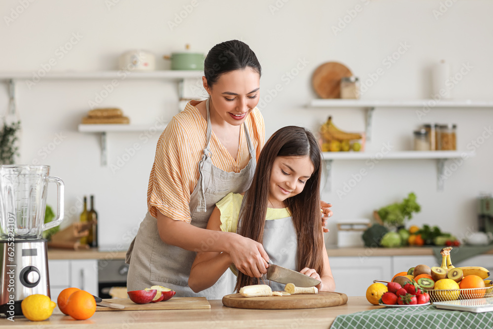 Little girl with her mother cutting banana for smoothie in kitchen