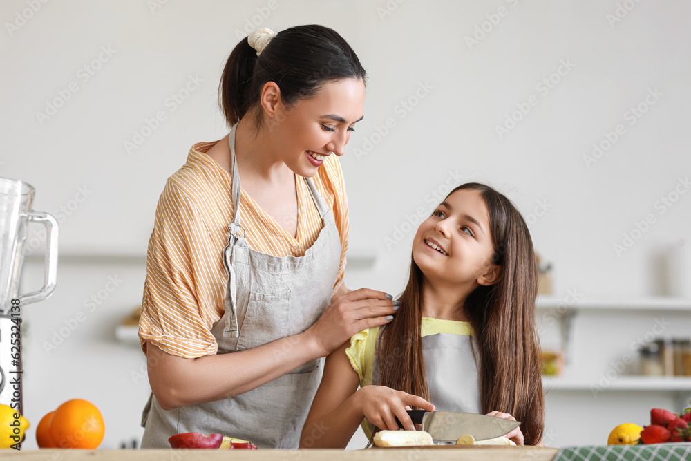 Little girl with her mother cutting banana for smoothie in kitchen