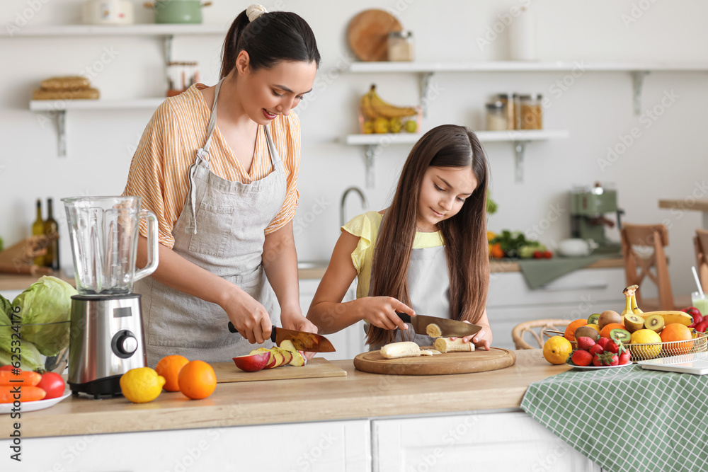 Little girl with her mother cutting banana for smoothie in kitchen