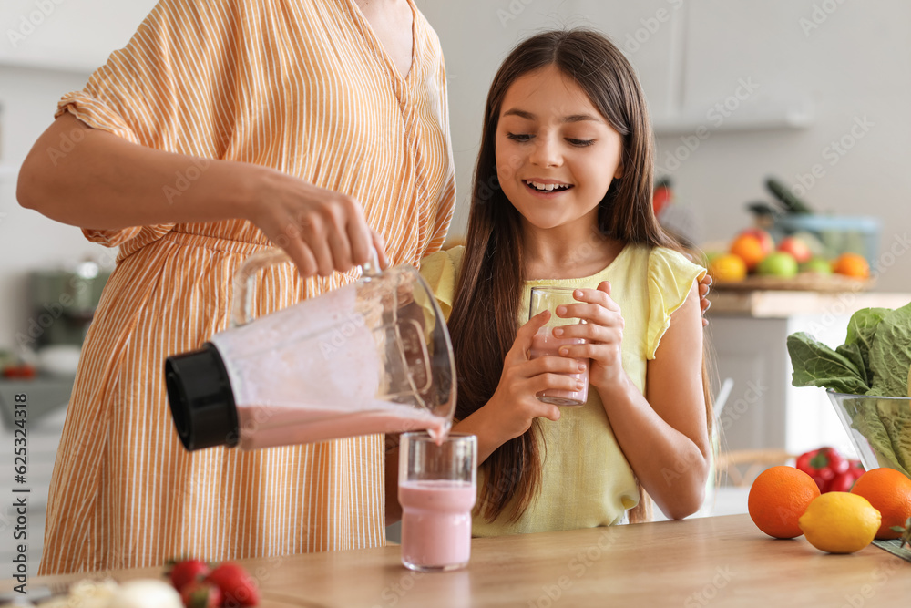 Young woman with her little daughter pouring fresh smoothie into glass in kitchen