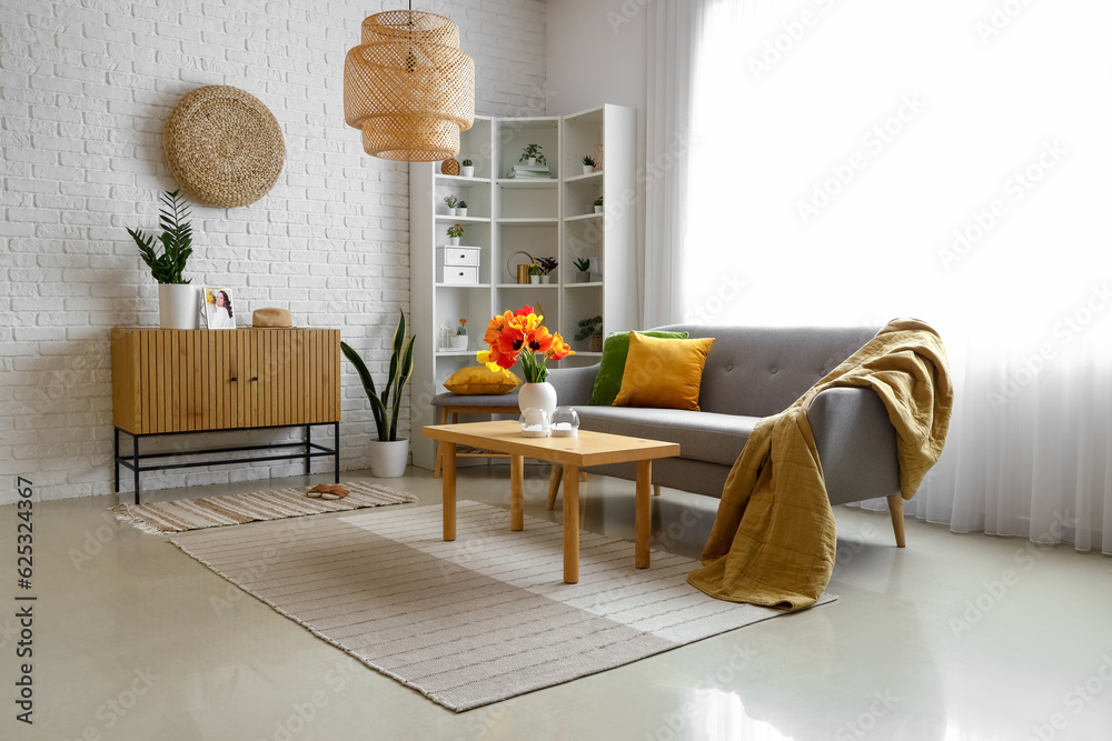 Interior of light living room with cozy grey sofa and tulip flowers on coffee table