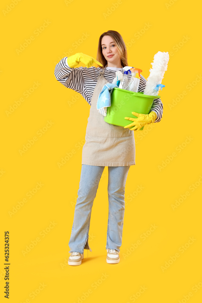 Young woman pointing at cleaning supplies on yellow background