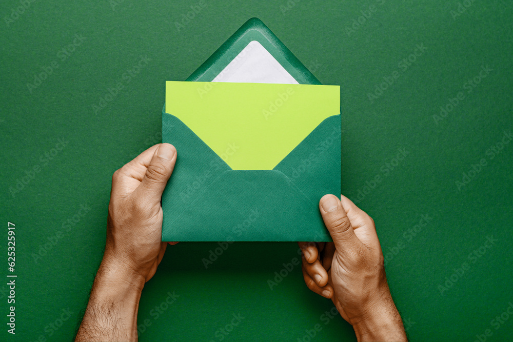 Male hands with envelope and blank card on green background, closeup