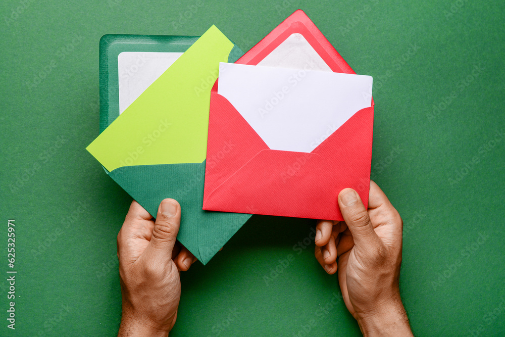 Male hands with envelopes and blank cards on green background, closeup