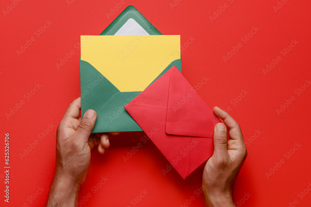 Male hands with envelopes and blank card on red background, closeup