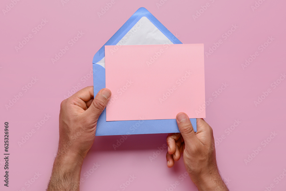 Male hands with envelope and blank card on pink background, closeup