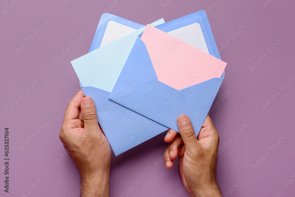 Male hands with envelopes and blank cards on purple background, closeup