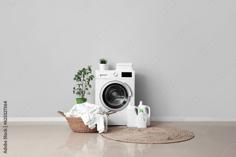 Washing machine, bottles of detergent and basket with dirty laundry near grey wall