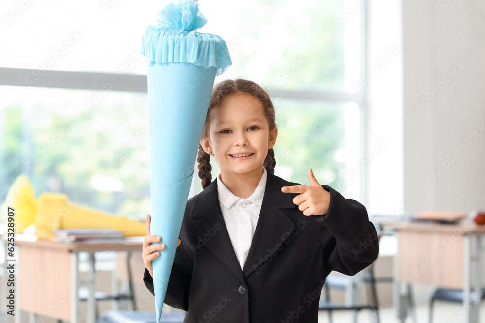 Happy little girl pointing at blue school cone in classroom