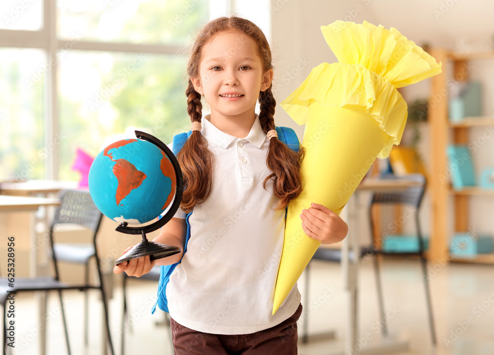 Happy little girl with yellow school cone and globe in classroom