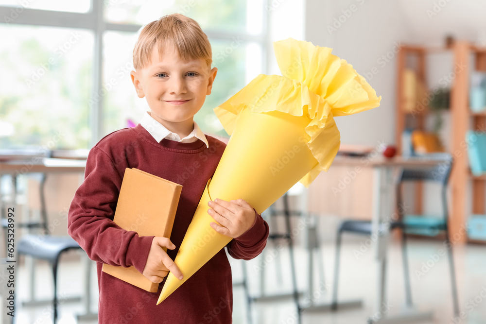 Happy little boy with yellow school cone and book in classroom