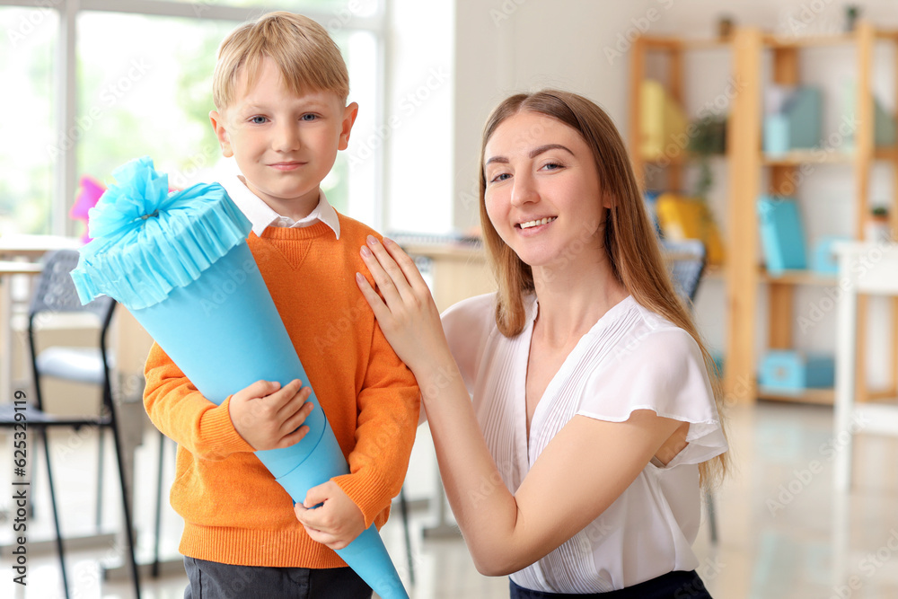 Happy little boy with blue school cone and teacher in classroom