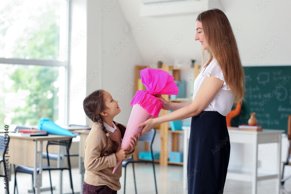 Happy little girl with pink school cone and teacher in classroom