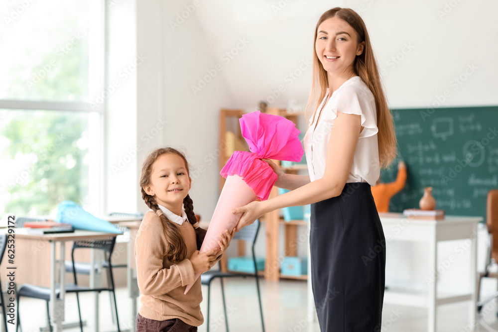 Happy little girl with pink school cone and teacher in classroom