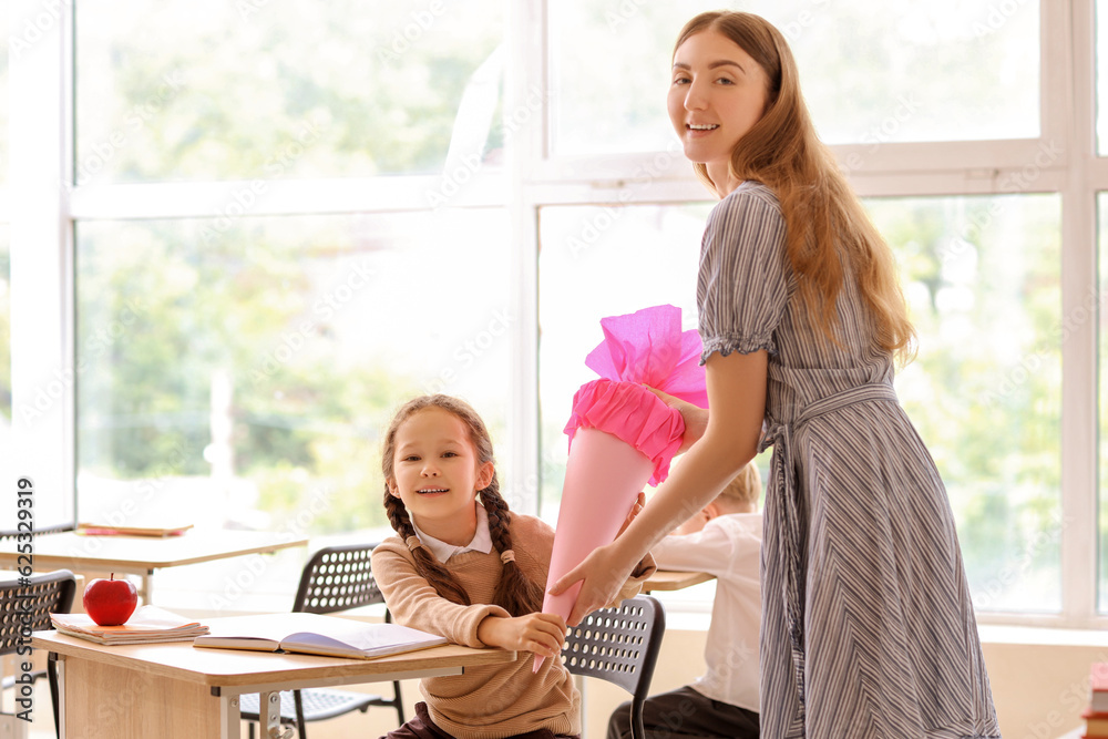 Teacher greeting her happy pupil with pink school cone in classroom