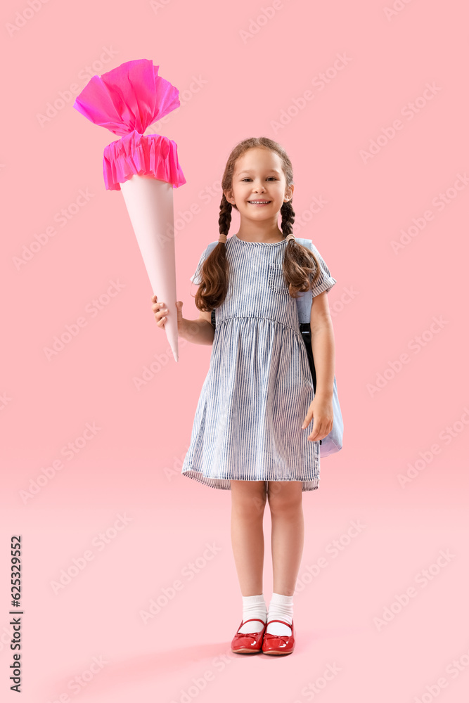 Happy little girl with backpack and school cone on pink background