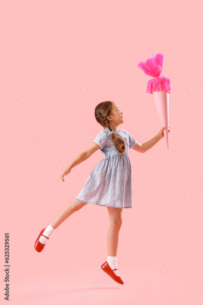 Happy little girl with school cone jumping on pink background