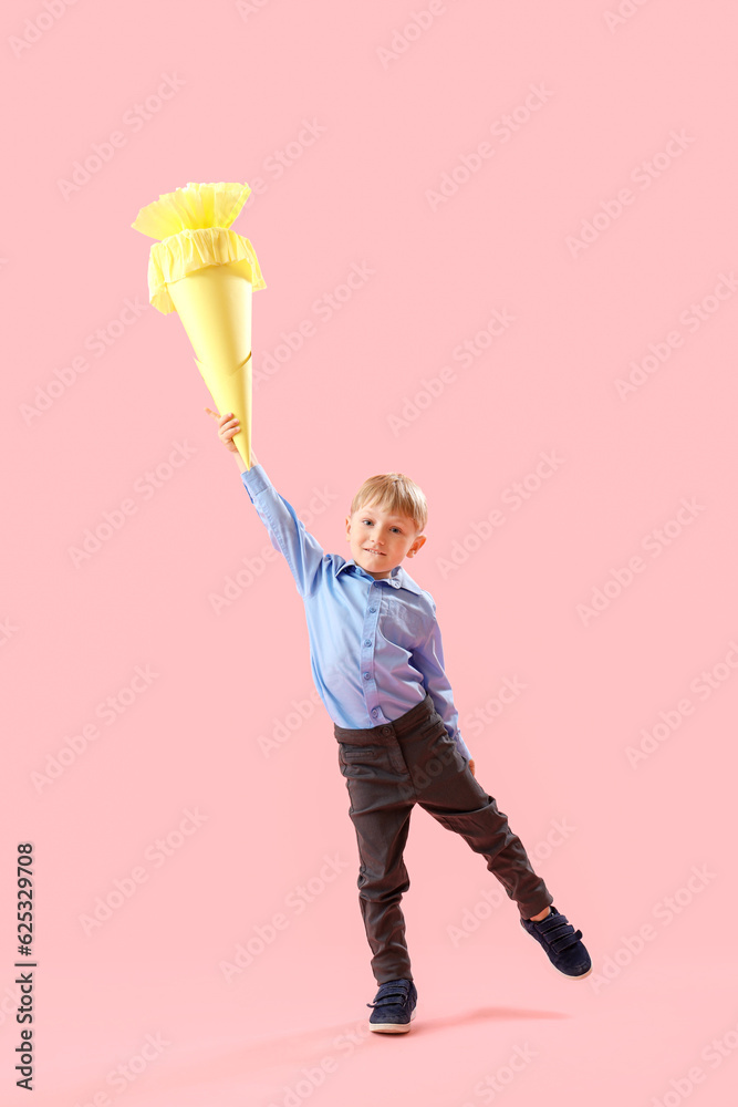 Happy little boy with yellow school cone jumping on pink background