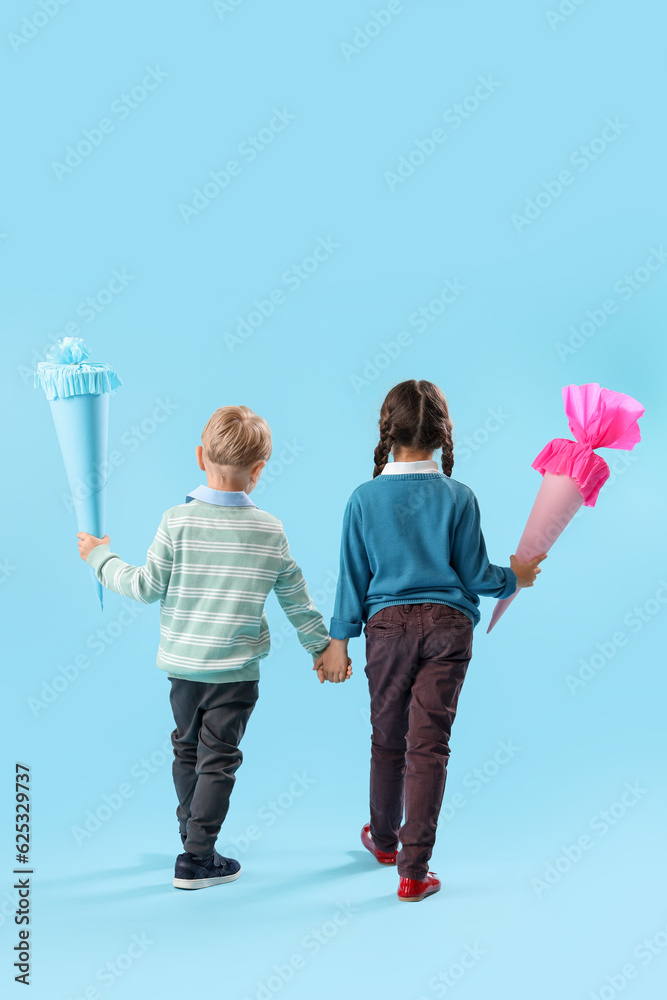 Little boy and girl with colorful school cones holding hands on blue background, back view