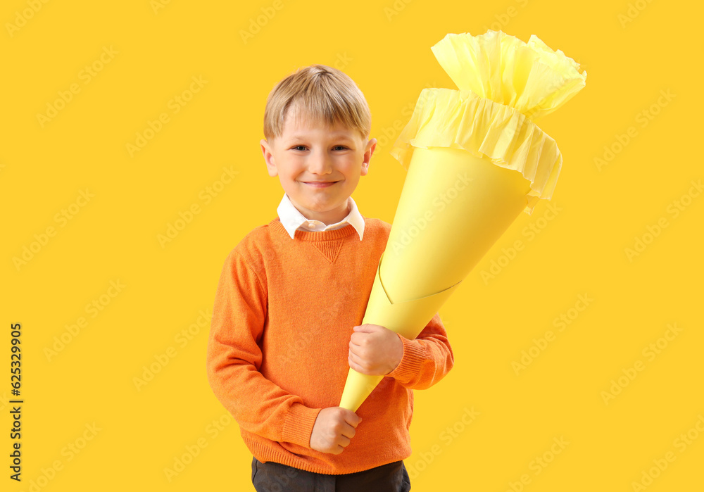 Happy little boy with school cone on yellow background