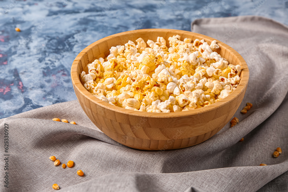 Bowl with tasty popcorn on blue background