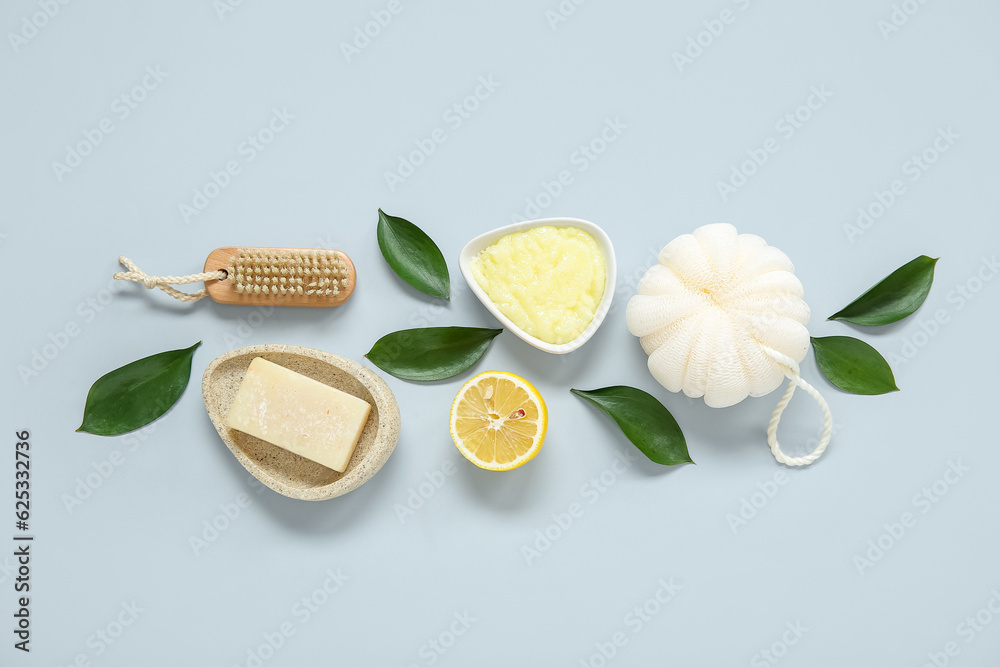 Bowl of lemon body scrub, bath sponge, massage brush and soap on grey background