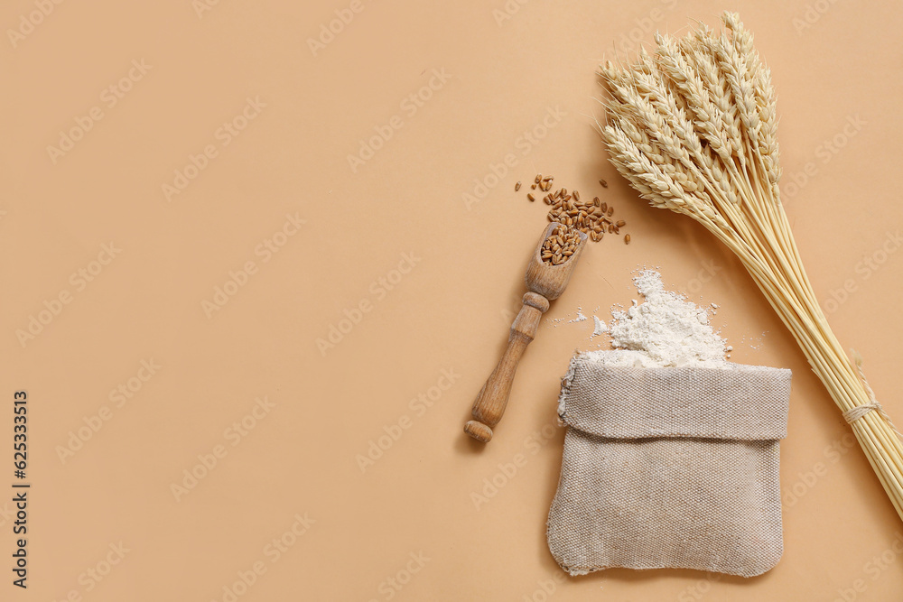 Bag of wheat flour, wooden scoop with grains and spikelets on beige background