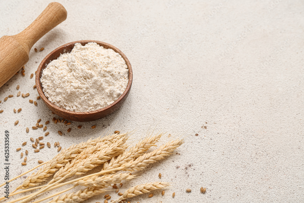 Wooden bowl with wheat flour and spikelets on grey background