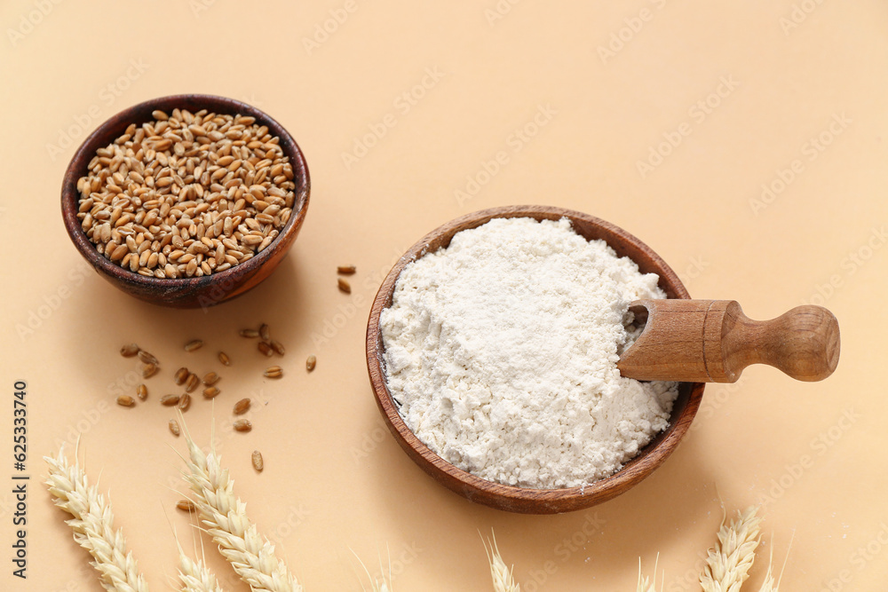 Bowls with wheat flour and grains on beige background