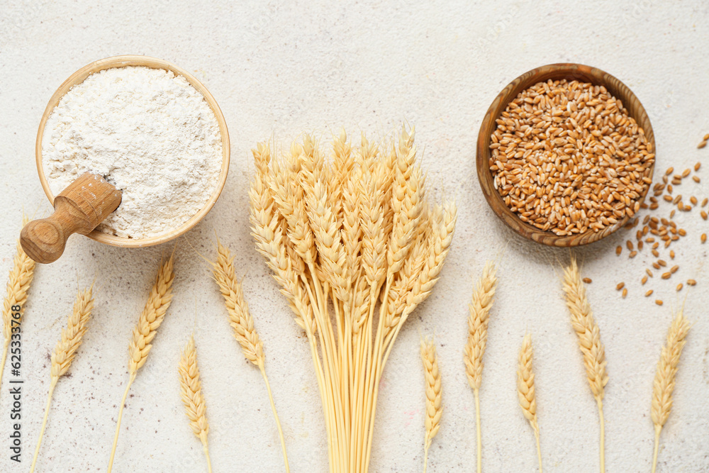 Bowls with wheat flour, grains and spikelets on grey background